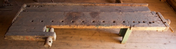 Høvelbenk i samlinga på Lundenes bygdetun. Benken er kring 185 cm lang og 60 cm brei over framtanga. Benken er bygd av ein planke som er 24 cm brei og 45 mm tjukk og går i heile lengda. Den har baktang av hjulmakartype og høvelbenkskuff som er omlag 20 cm brei. Foto: Roald Renmælmo
